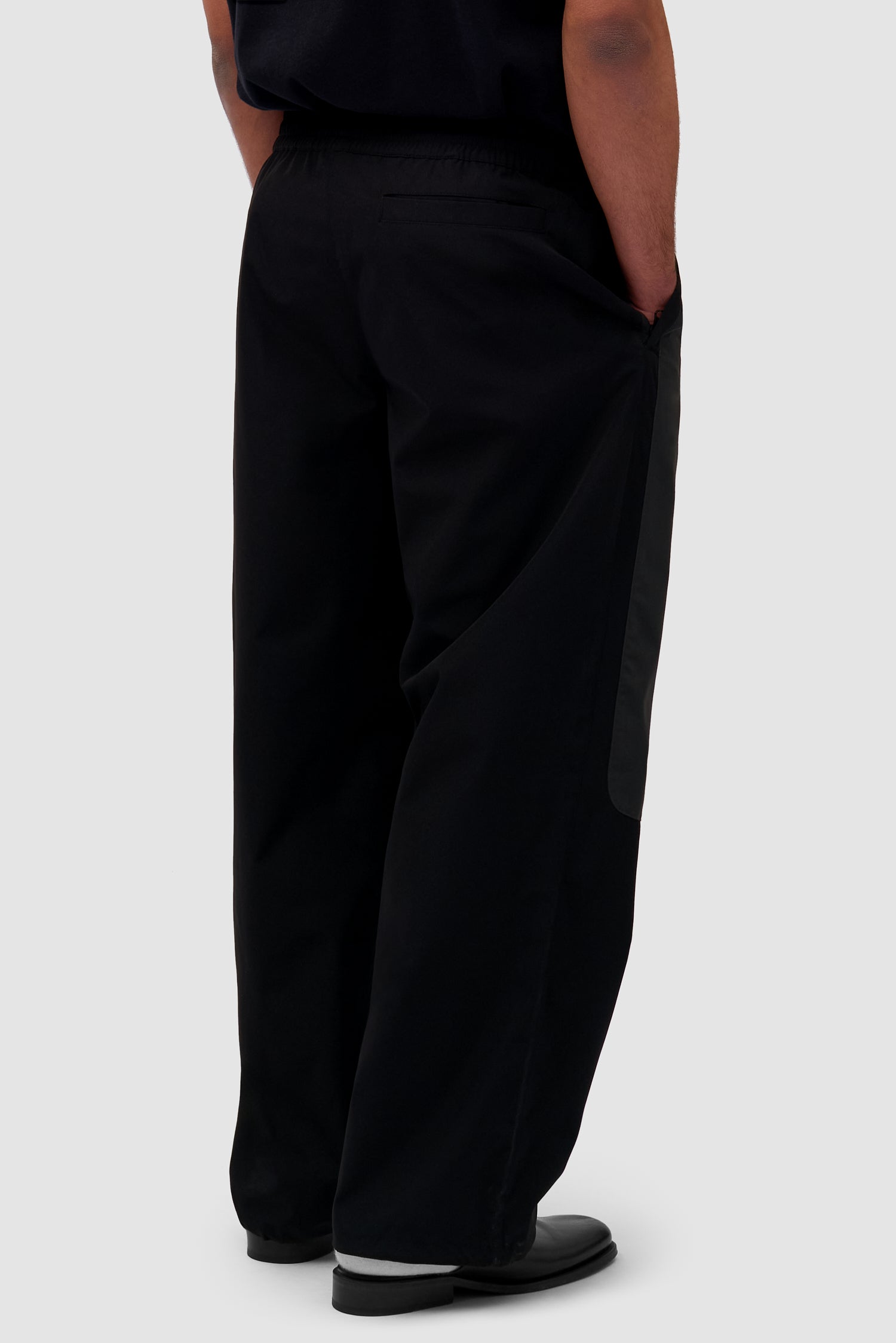 Tracksuit Pants in Black worn by a model, half-body back view