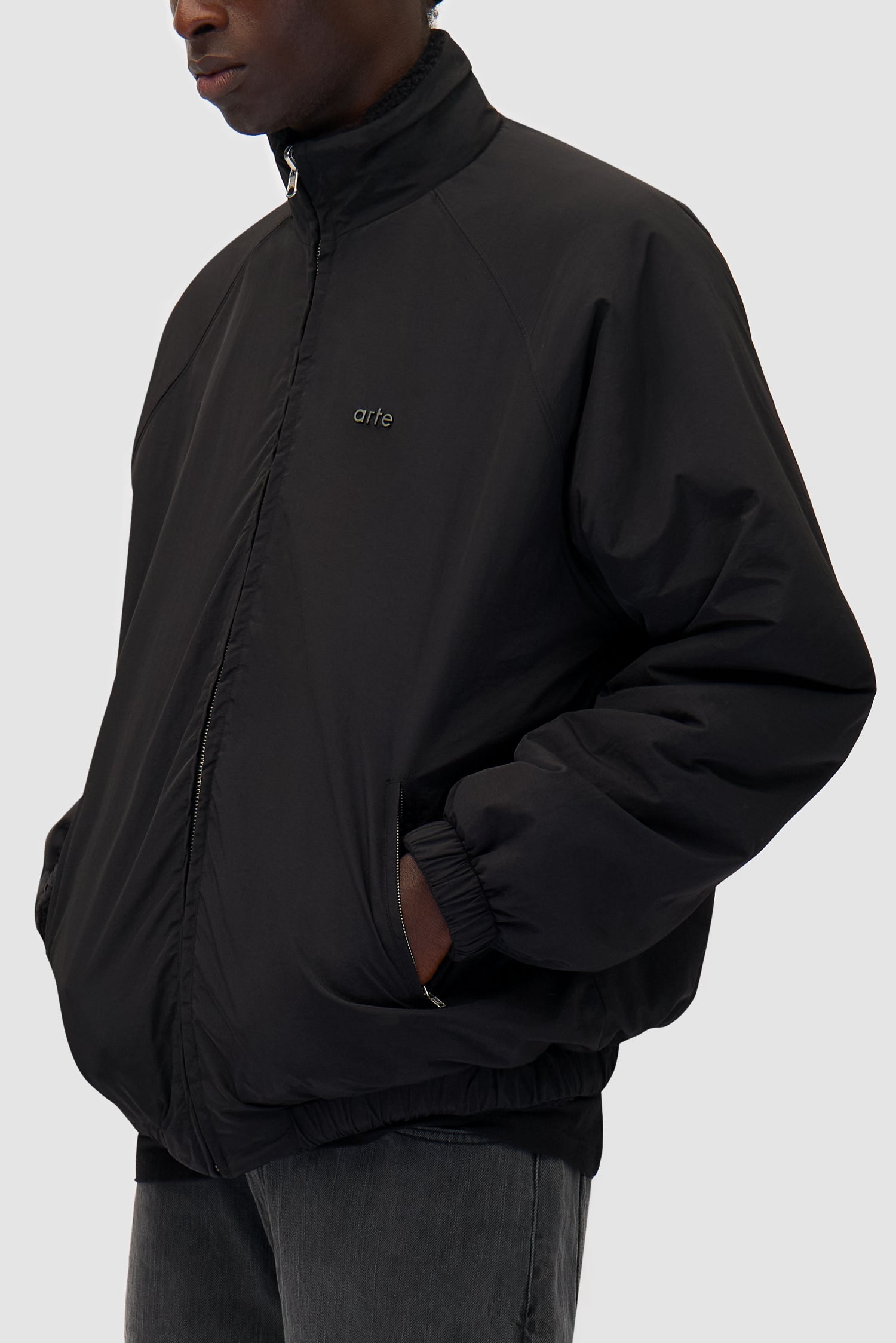 Reversible Polar Jacket in Black worn reversed by a model, half-body front view, logo detail
