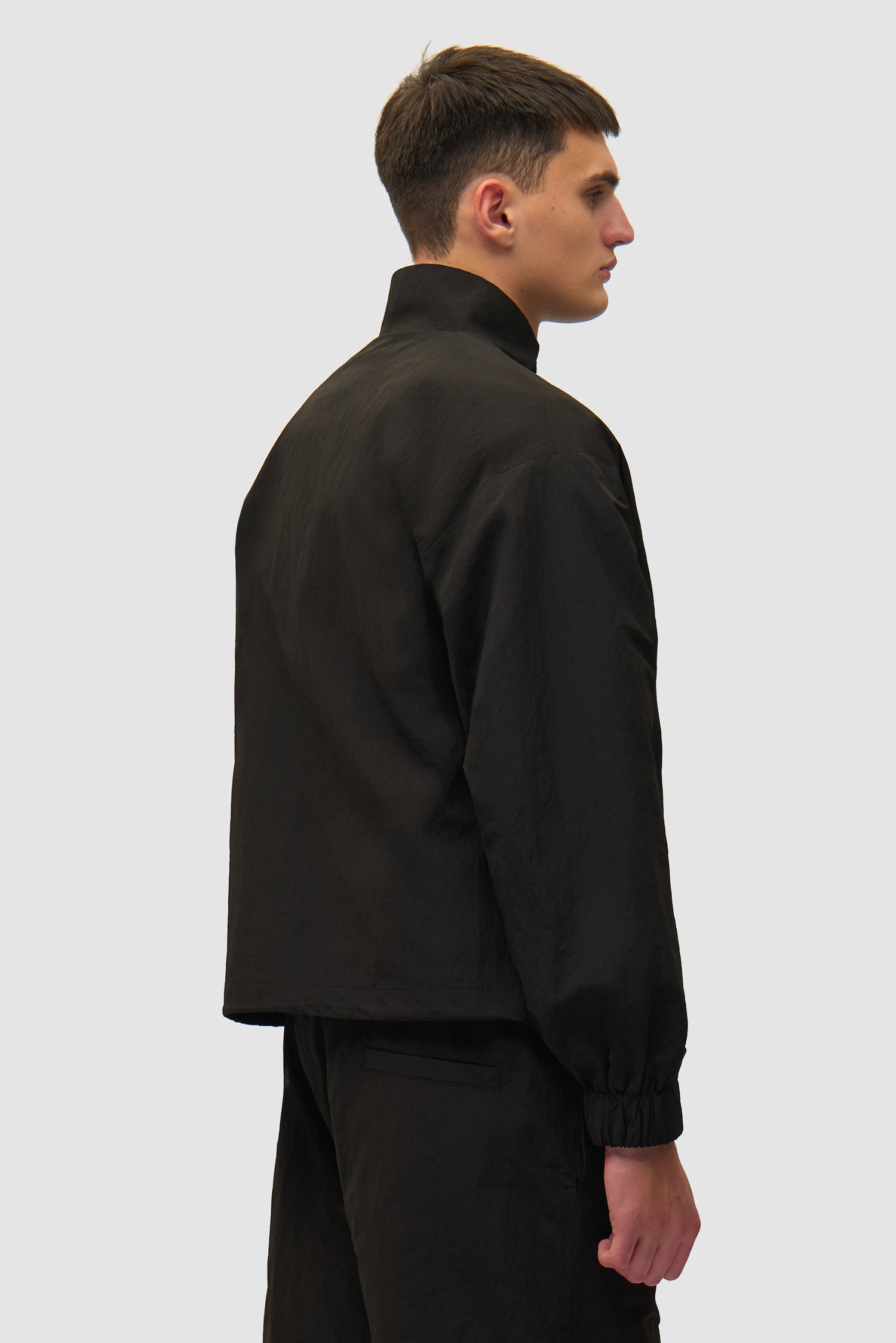 Veste de survêtement carrée noire portée par un mannequin, vue de dos à mi-corps