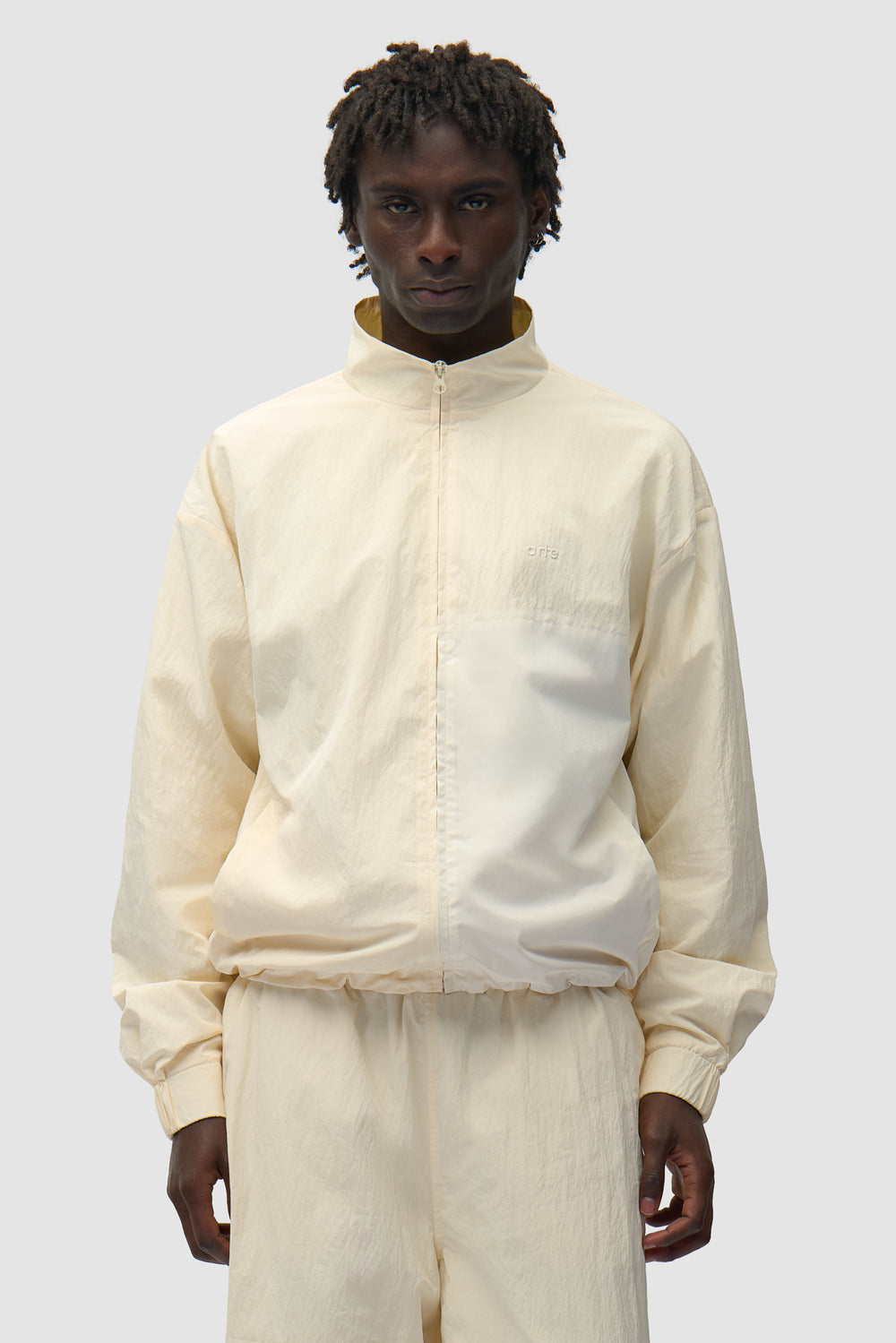 Veste de survêtement carrée couleur crème portée par un mannequin, vue de face en demi-corps