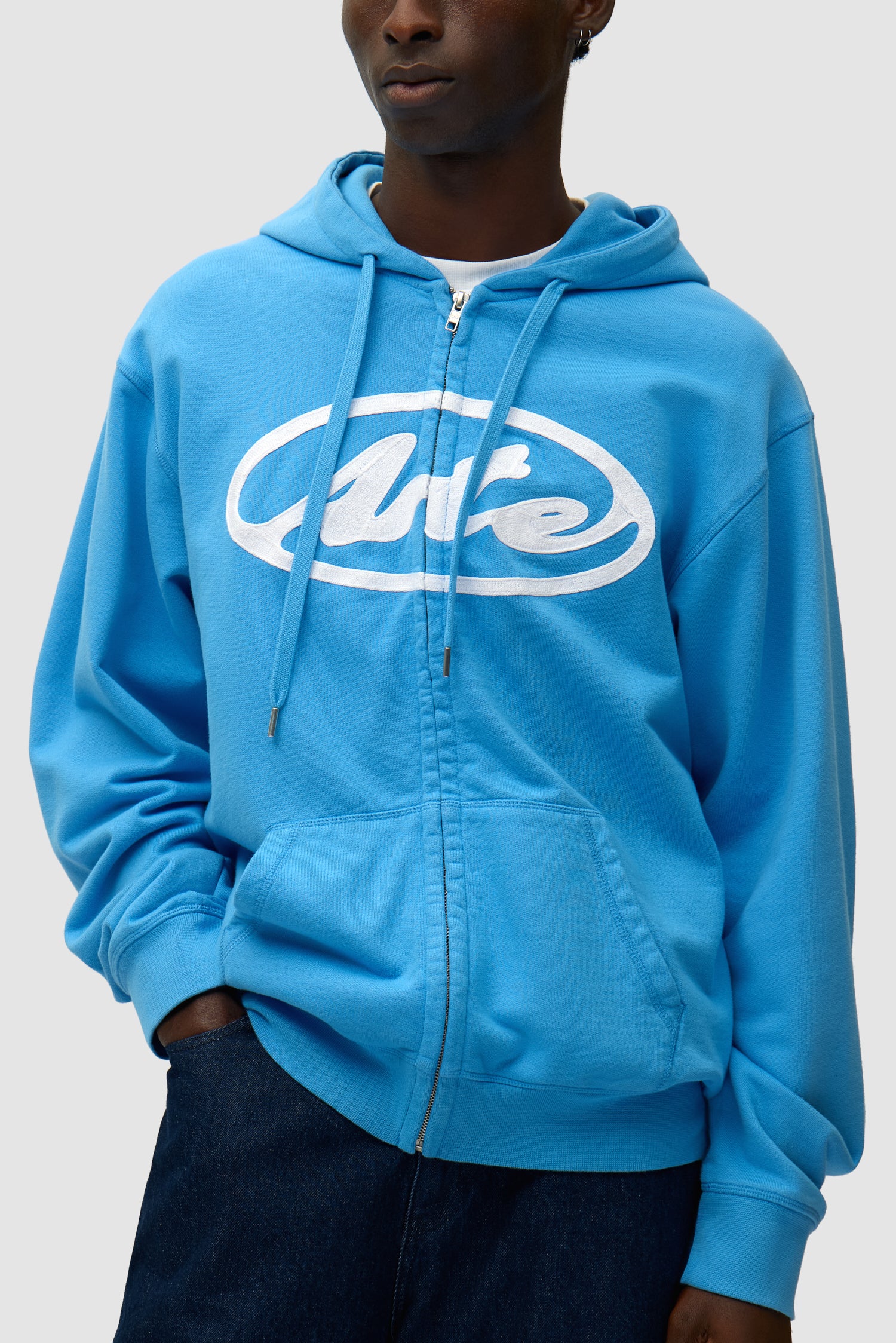 Sweat à capuche zippé avec logo circulaire, couleur bleue, porté par un mannequin, vue détaillée du haut du corps