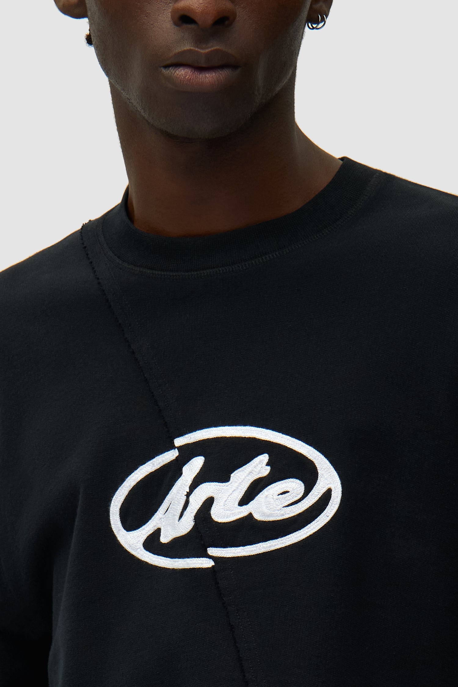 Vue détaillée du pull noir brodé d'un logo circulaire, montrant le logo sur le devant.