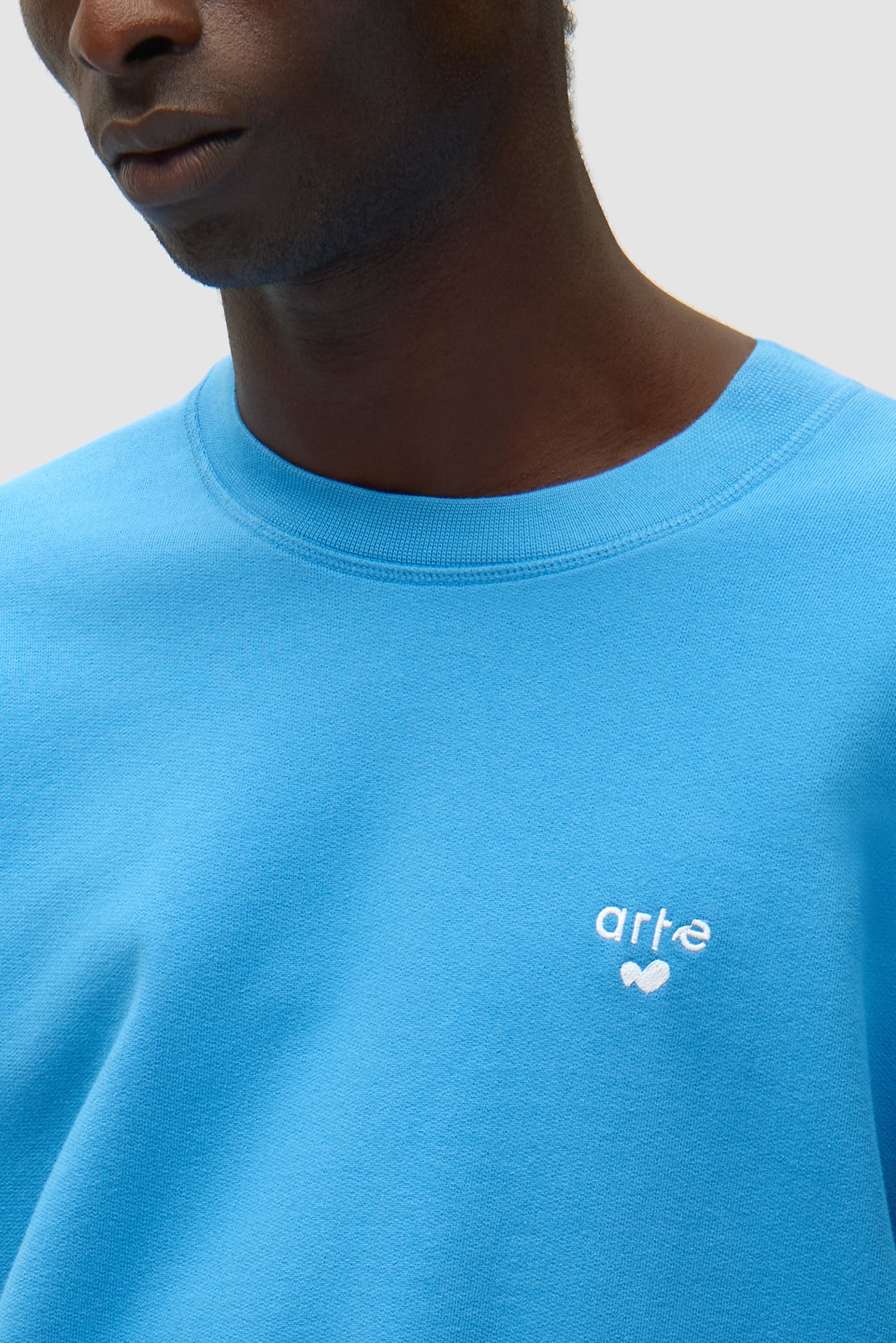 Vue détaillée du t-shirt à col rond bleu avec logo en forme de cœur, montrant le logo