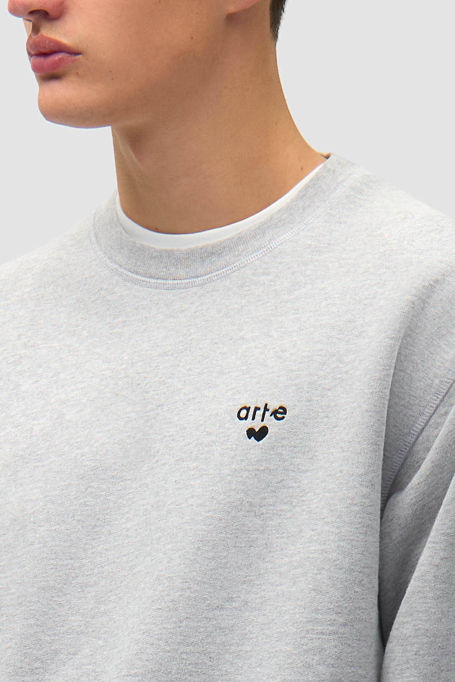 Vue détaillée du sweat à col rond gris avec logo en forme de cœur, montrant le logo