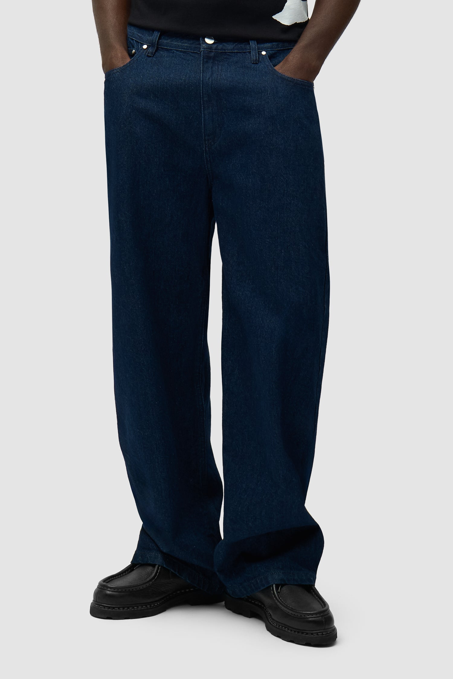 Pantalon à poche avec logo circulaire en denim brut porté par un mannequin, vue de face en demi-corps