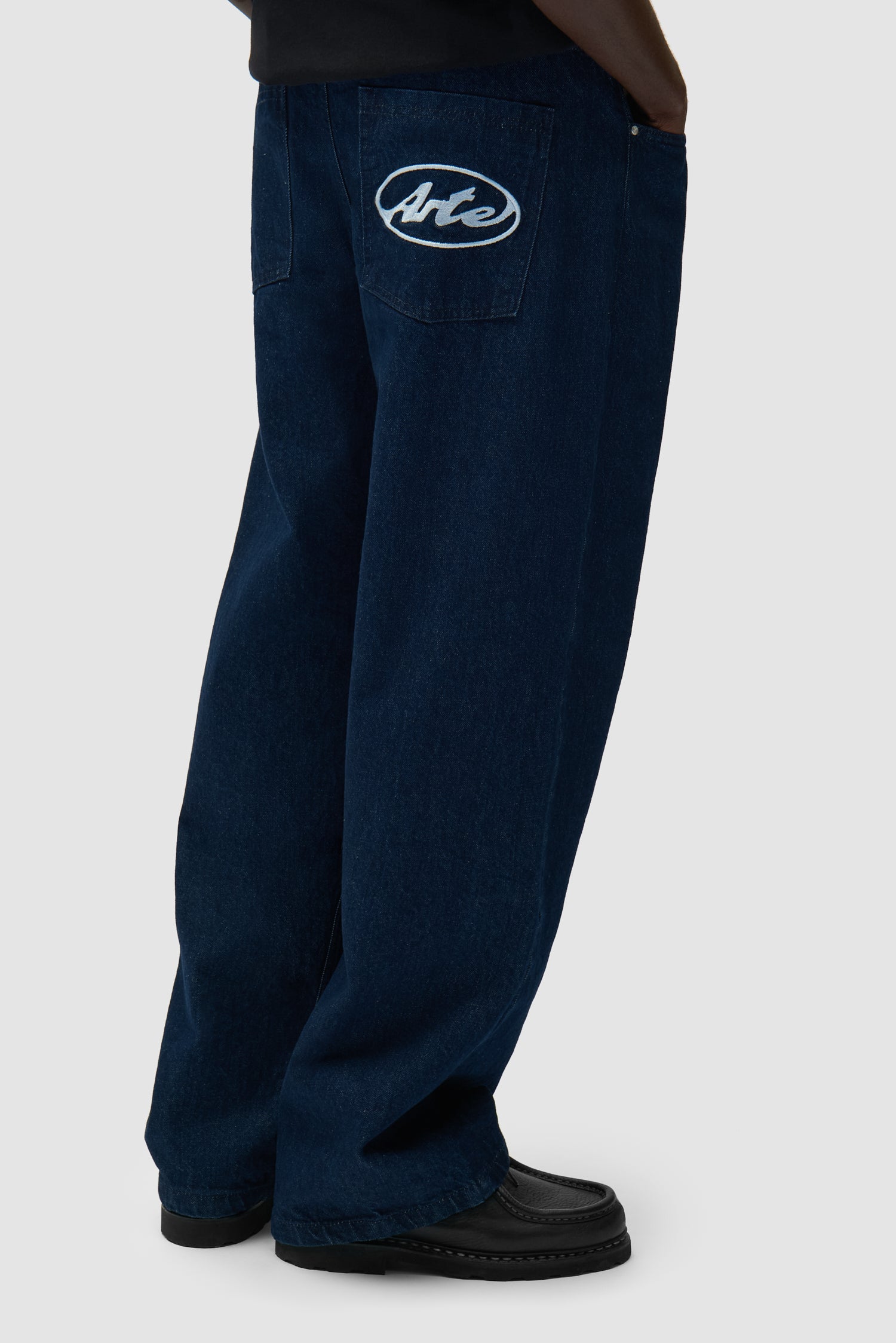 Pantalon à poche avec logo circulaire en denim brut porté par un mannequin, vue de profil