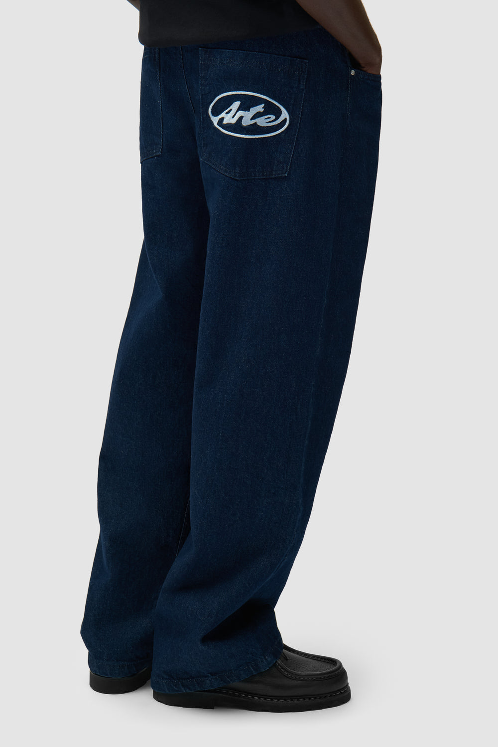 Pantalon à poche avec logo circulaire en denim brut porté par un mannequin, vue de profil