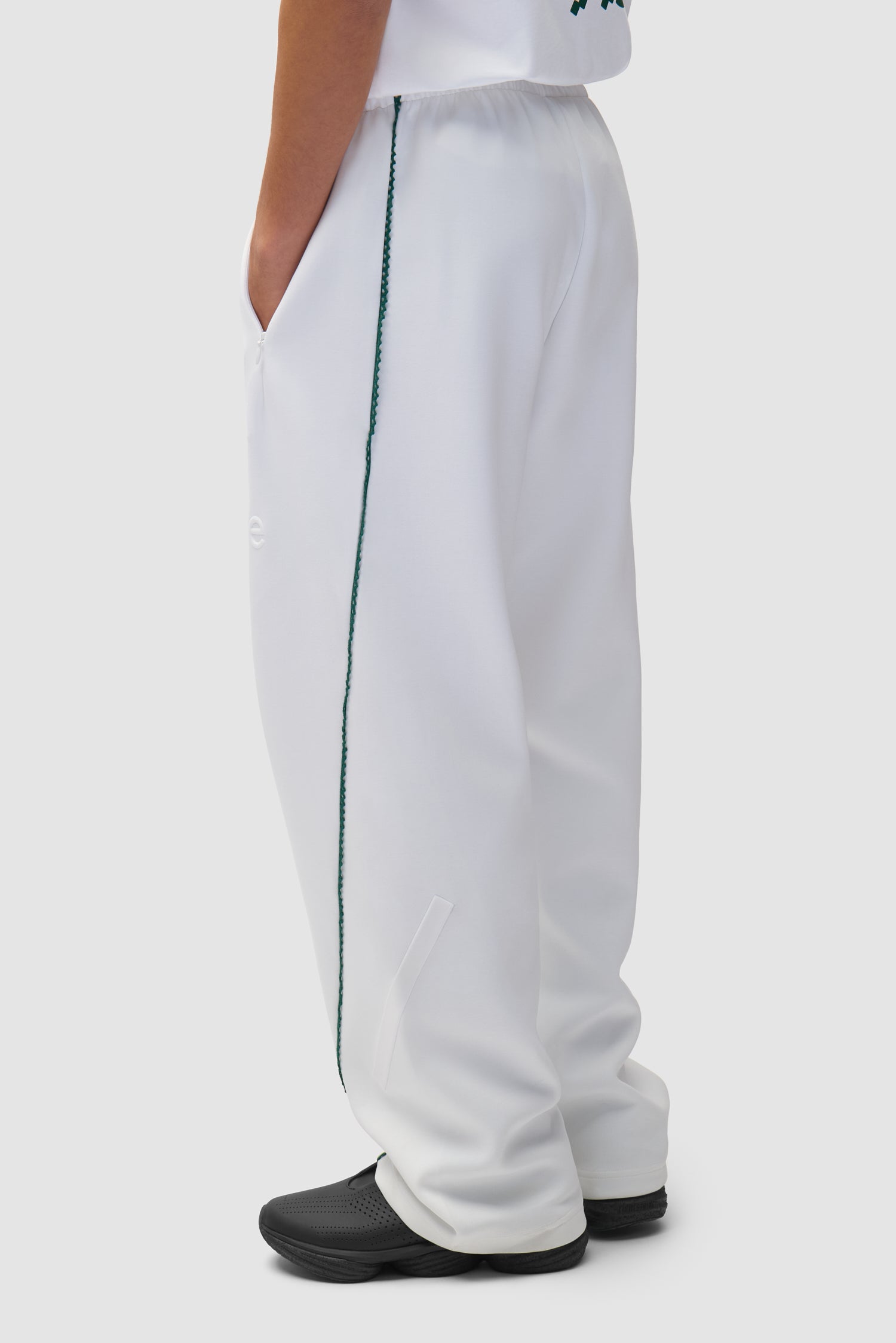 Pantalon Arte pour adidas Z.N.E. en blanc/Better Scarlet porté par un mannequin, vue de profil à mi-corps