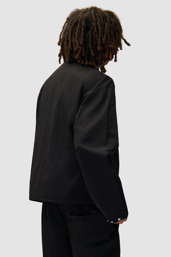 Nylon Track Jacket in Black worn by a model, half-body back view
