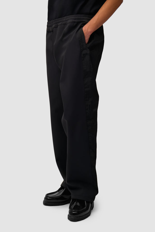 Nylon Track Pants in Black worn by a model, half-body side view