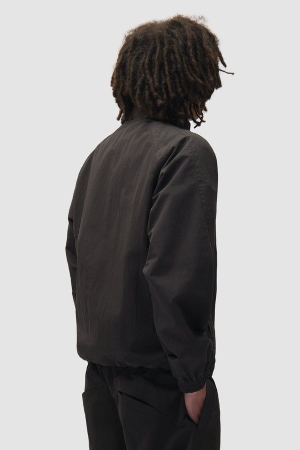 Uniform Track Jacket in Black worn by a model, half-body back view