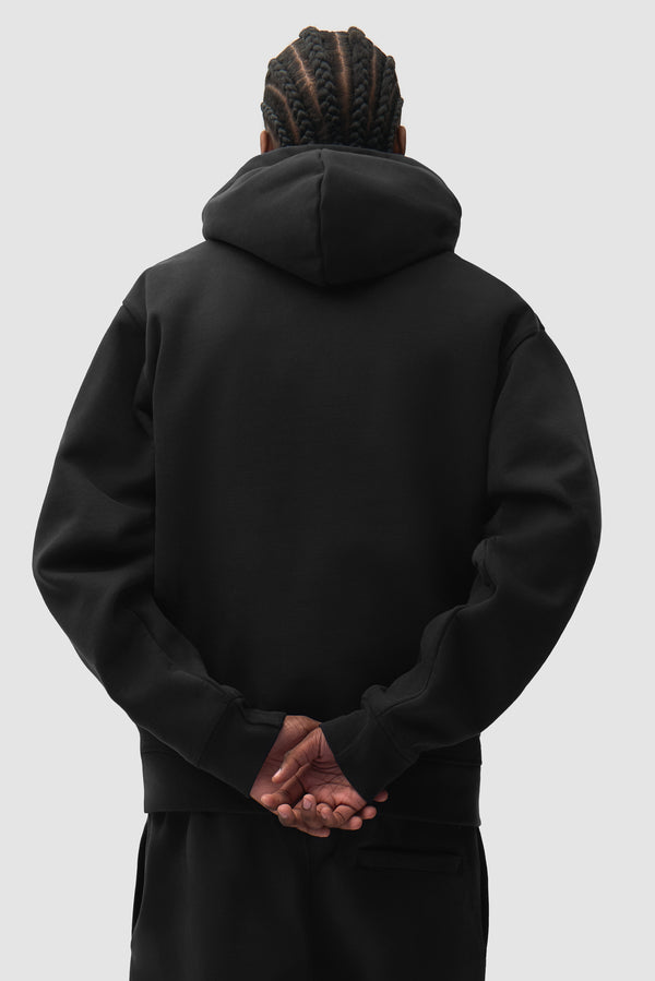 Cor Hoodie in Black worn by a model, half-body back view