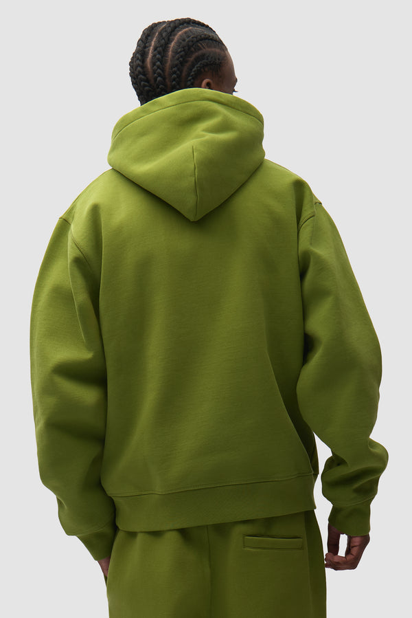 Cor Hoodie in Green worn by a model, half-body back view