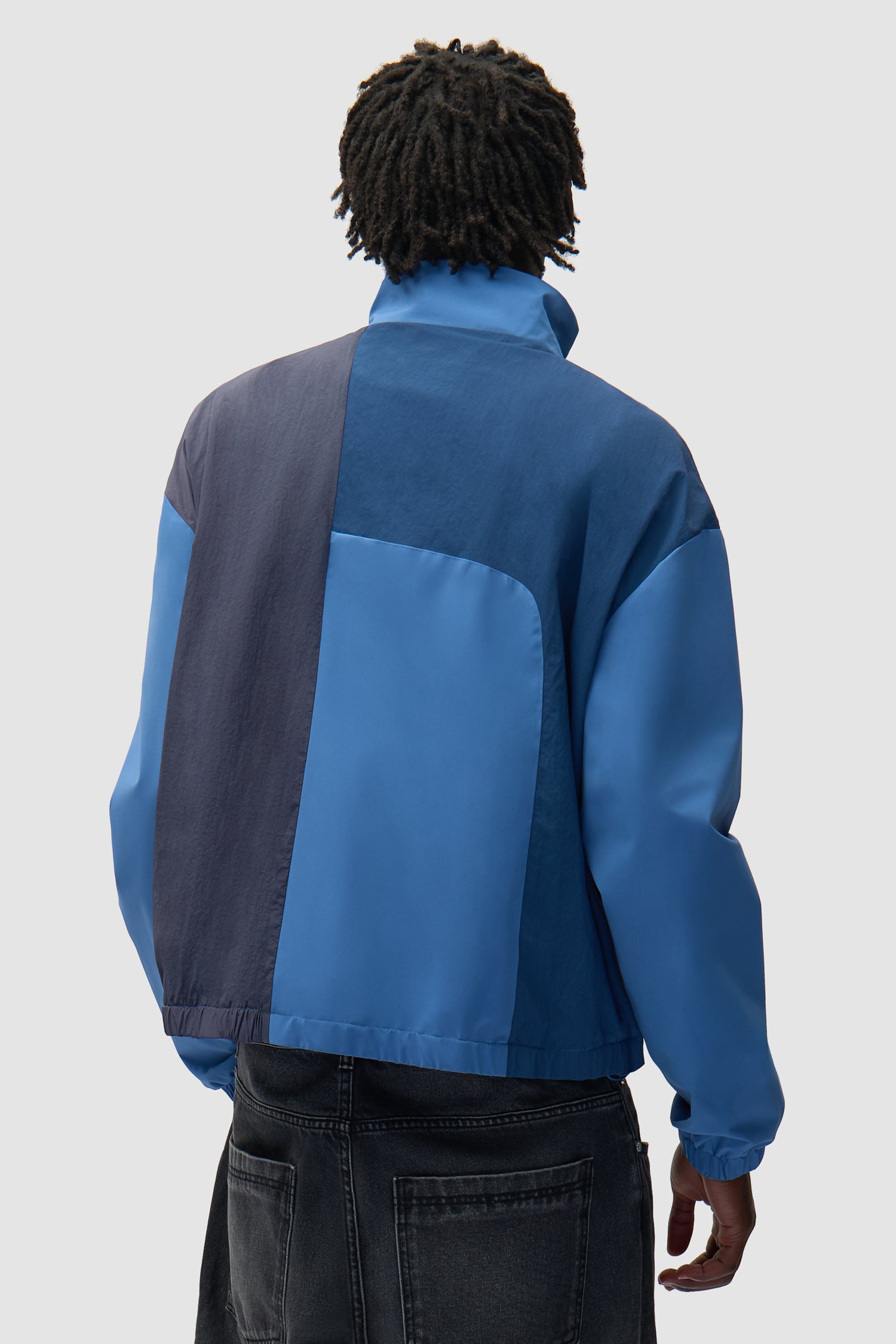 Veste zippée courbée bleue portée par un mannequin, vue de dos à mi-corps