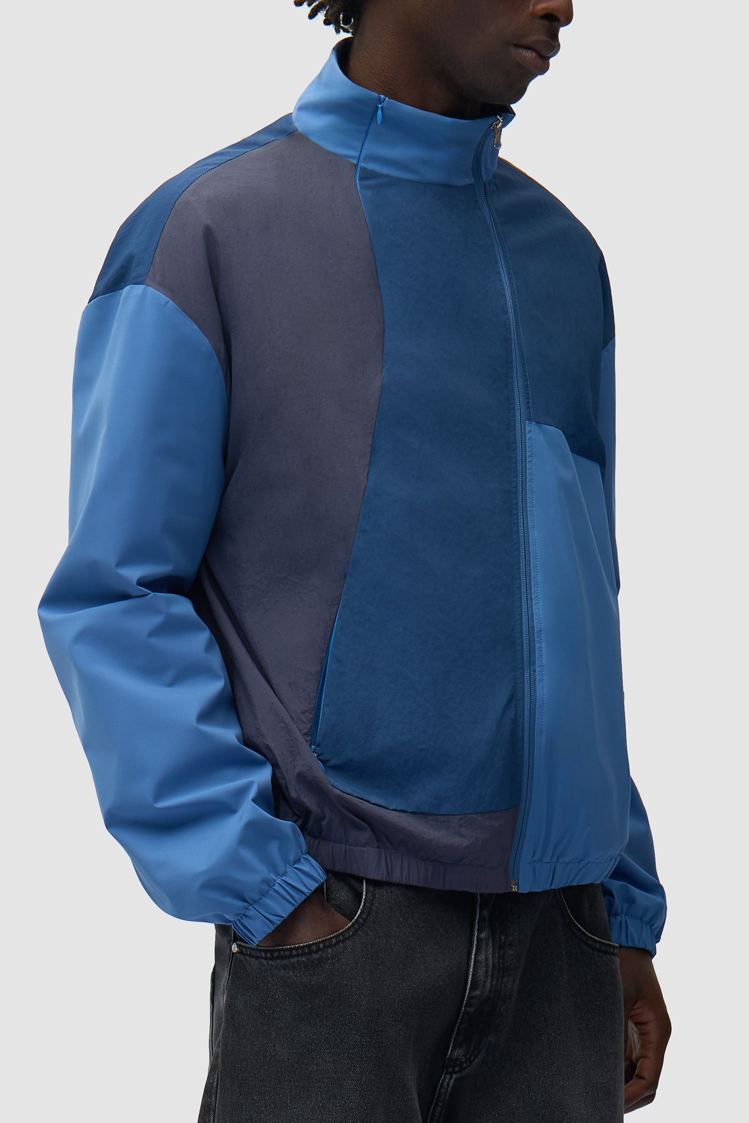 Veste zippée courbée bleue portée par un mannequin, vue de profil à mi-corps