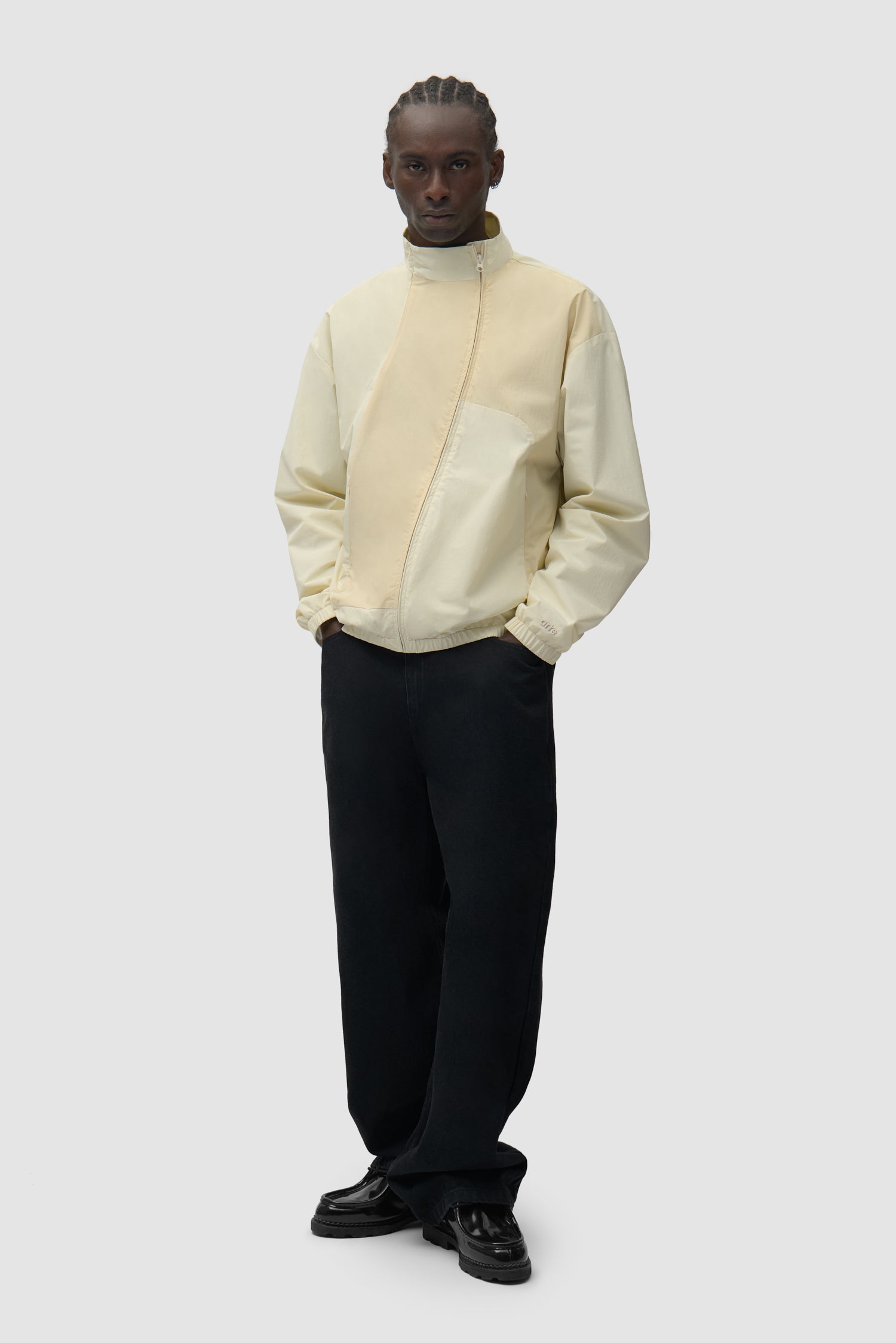 Veste zippée courbée couleur crème portée par un mannequin, vue de face en pied