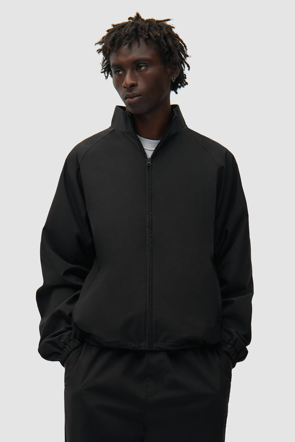 Veste de survêtement de marque noire portée par un mannequin, vue de face en demi-corps