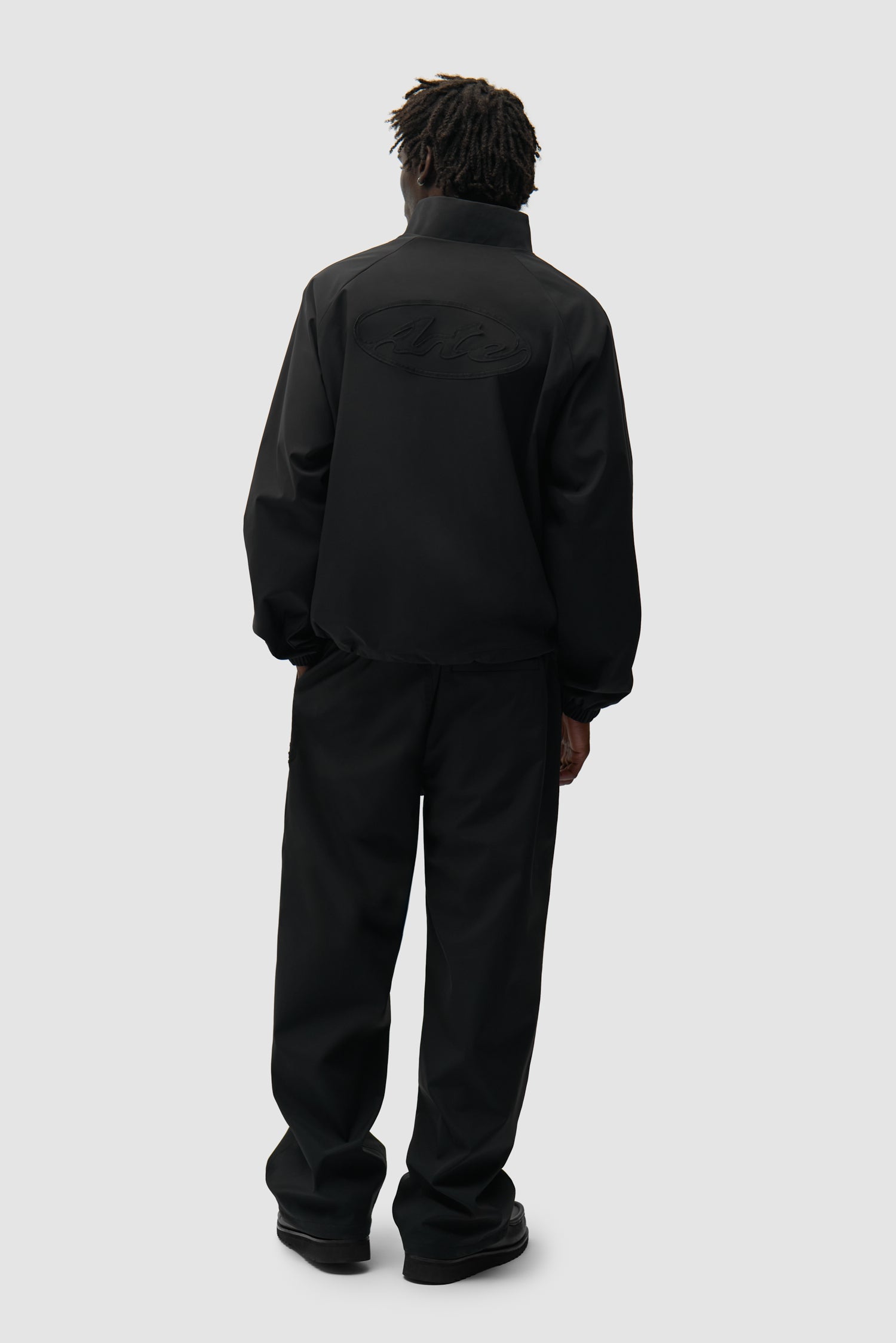 Branded Trackjacket in Black worn by a model, full-body back view