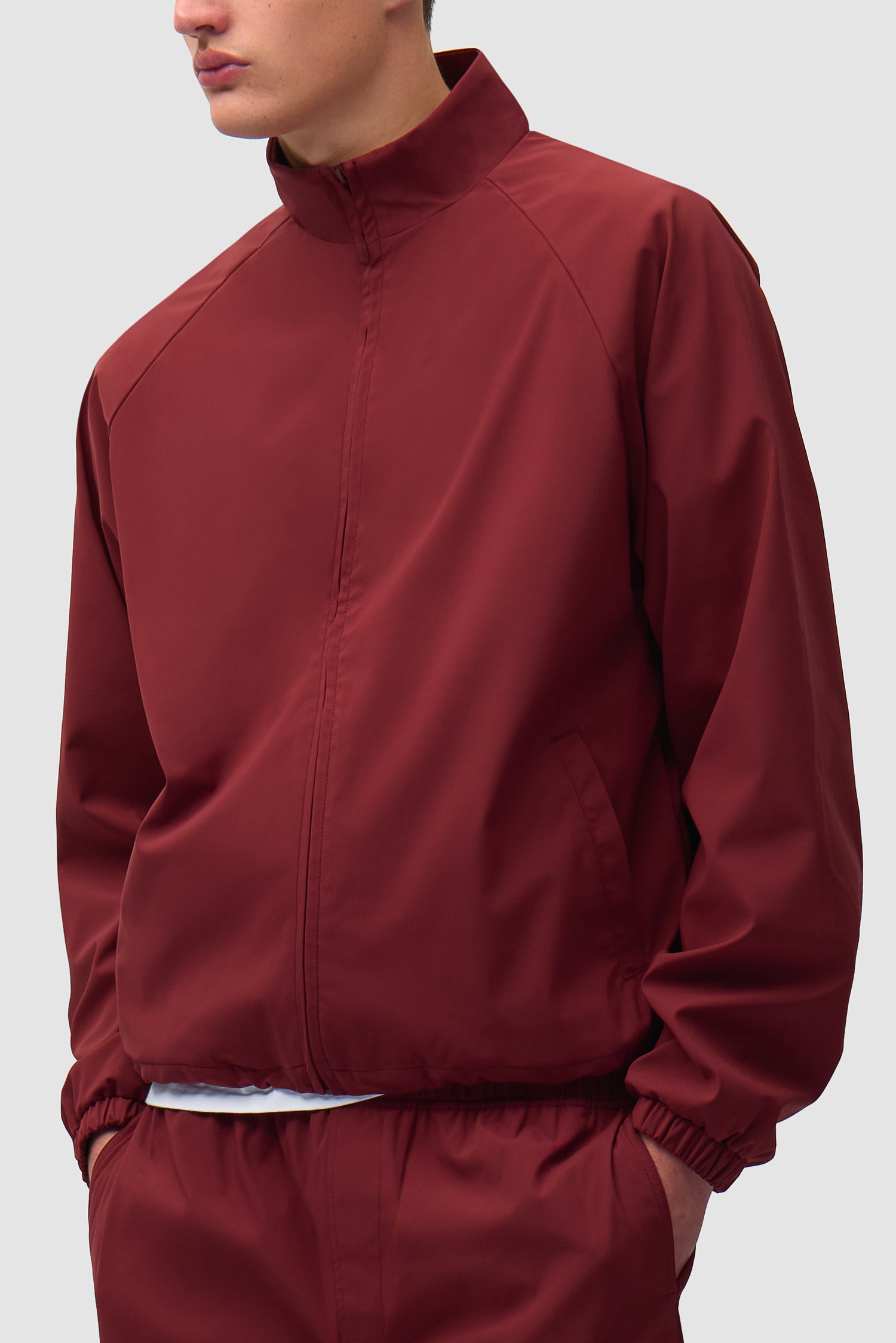 Veste de survêtement de marque bordeaux portée par un mannequin, vue de profil à mi-corps