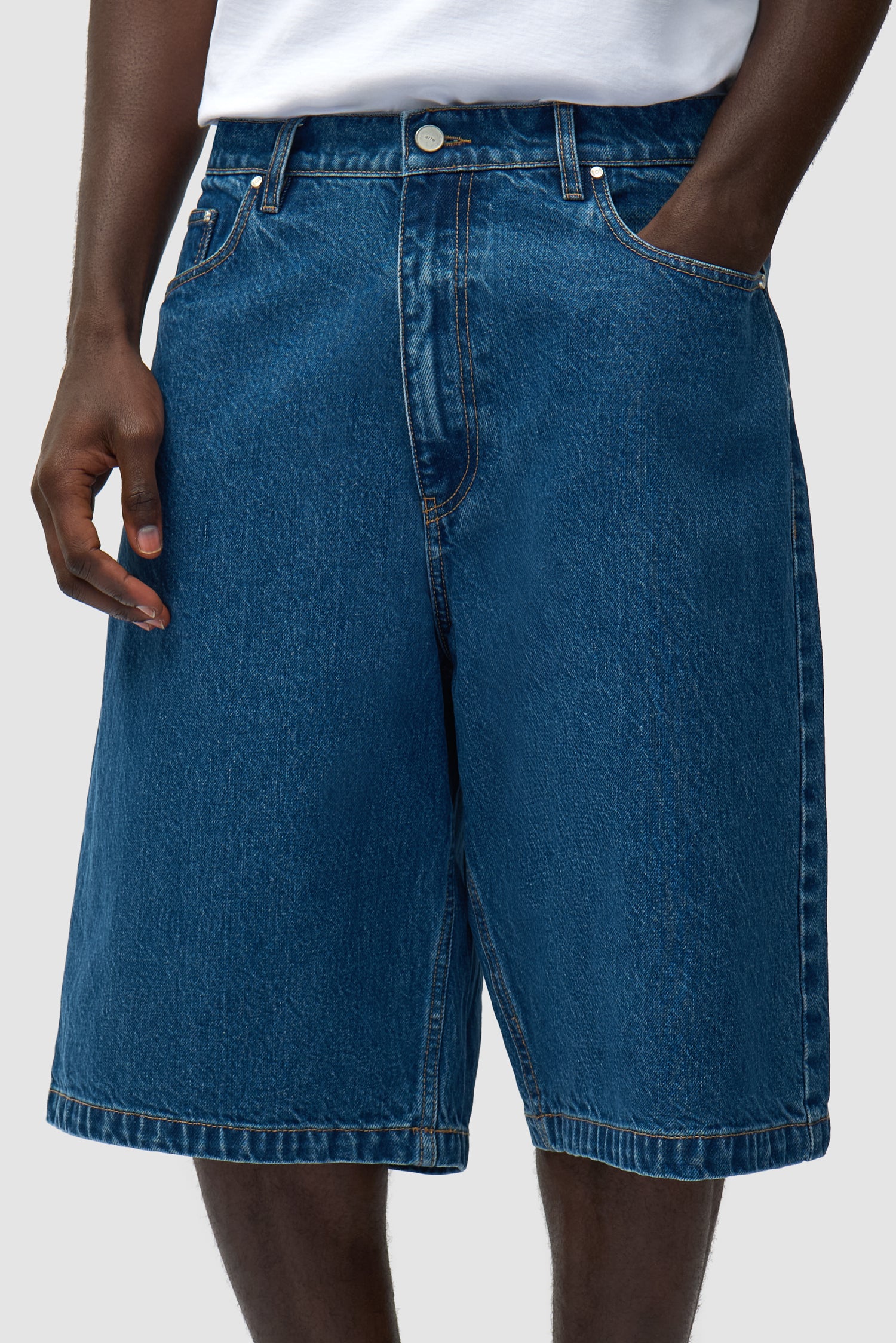 Short en denim à poche ronde en denim brut porté par un mannequin, vue de profil en pied