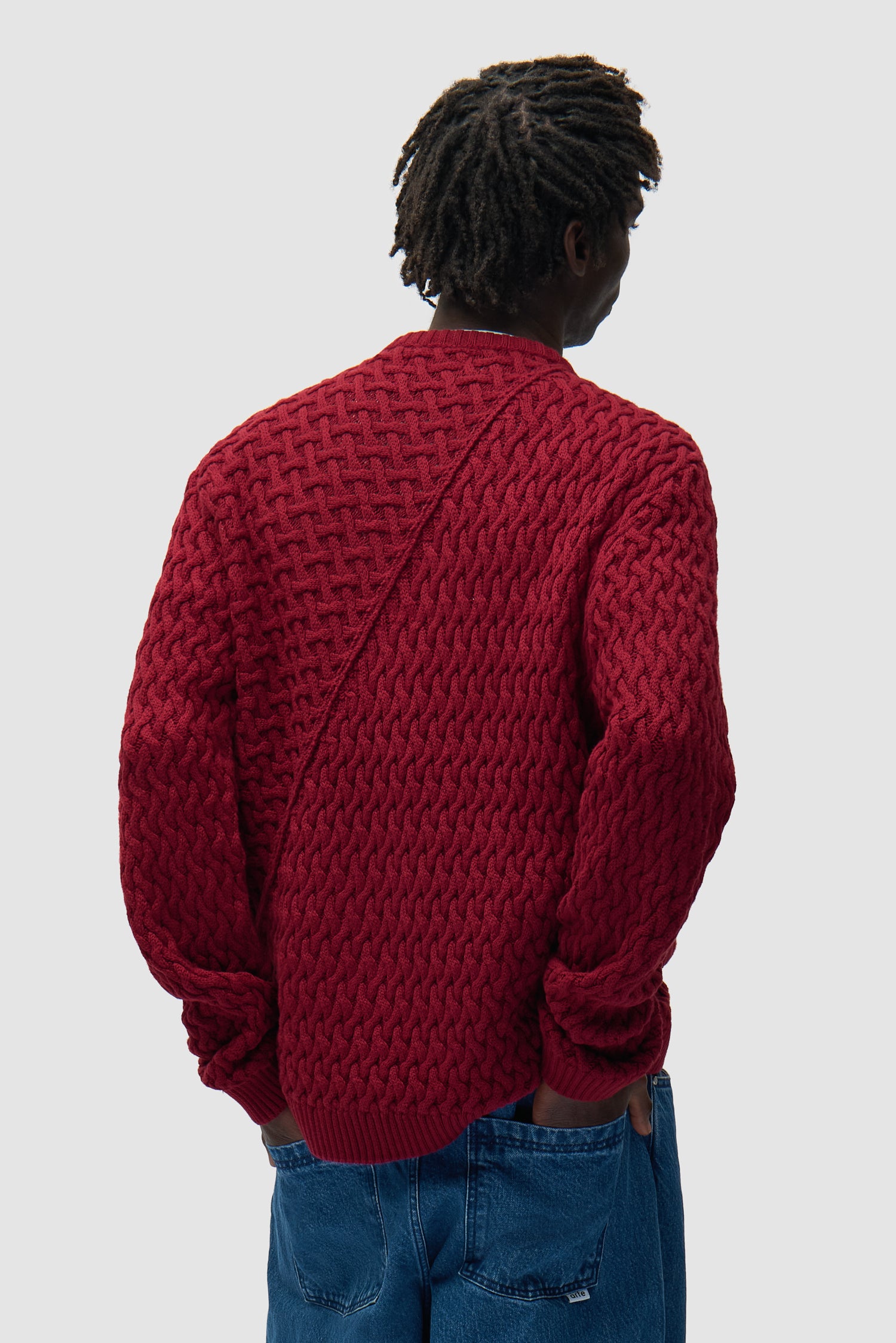 Pull à logo déformé couleur bordeaux porté par un mannequin, vue de dos à mi-corps