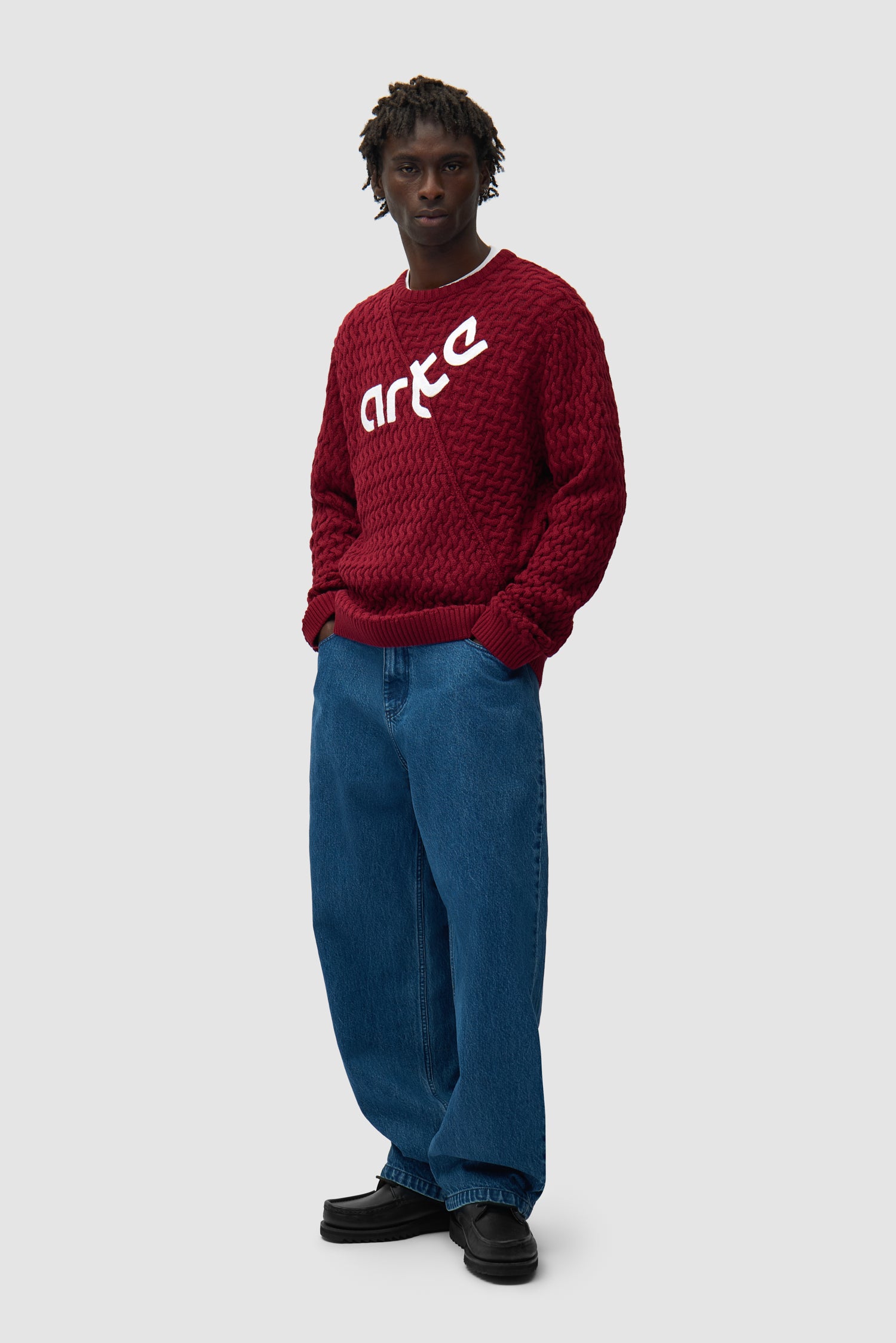 Pull à logo déformé couleur bordeaux porté par un mannequin, vue de profil en pied