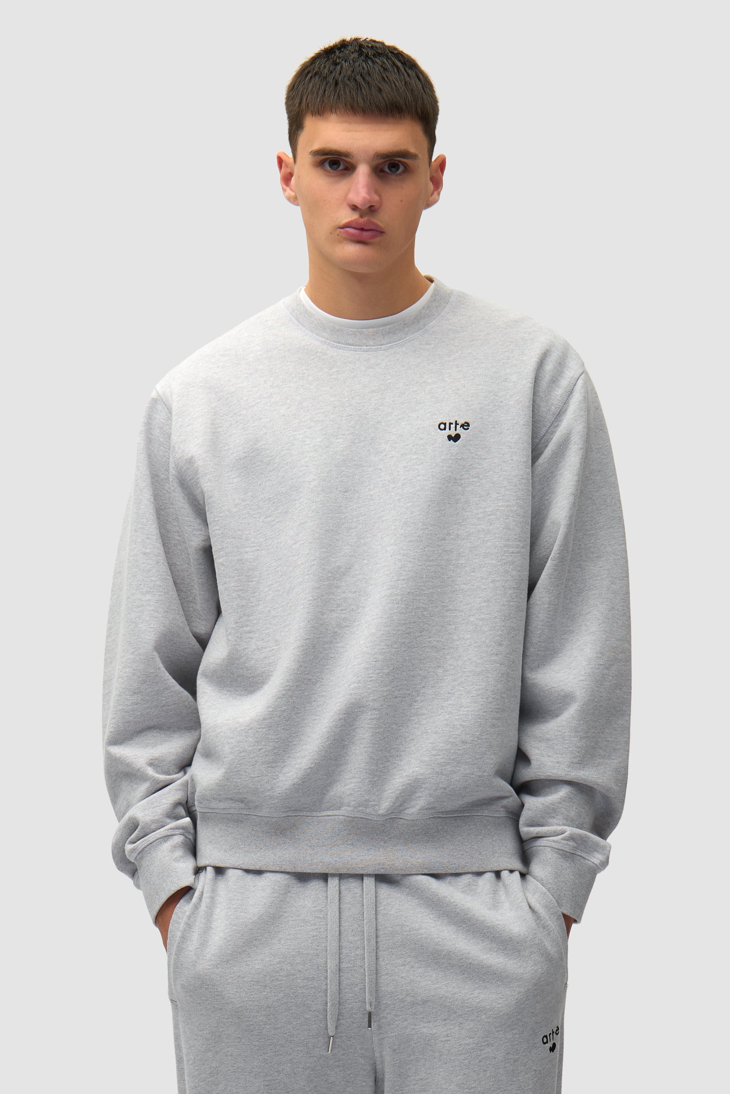 T-shirt à col rond avec logo en forme de cœur, couleur grise, porté par un mannequin, vue de face, demi-corps