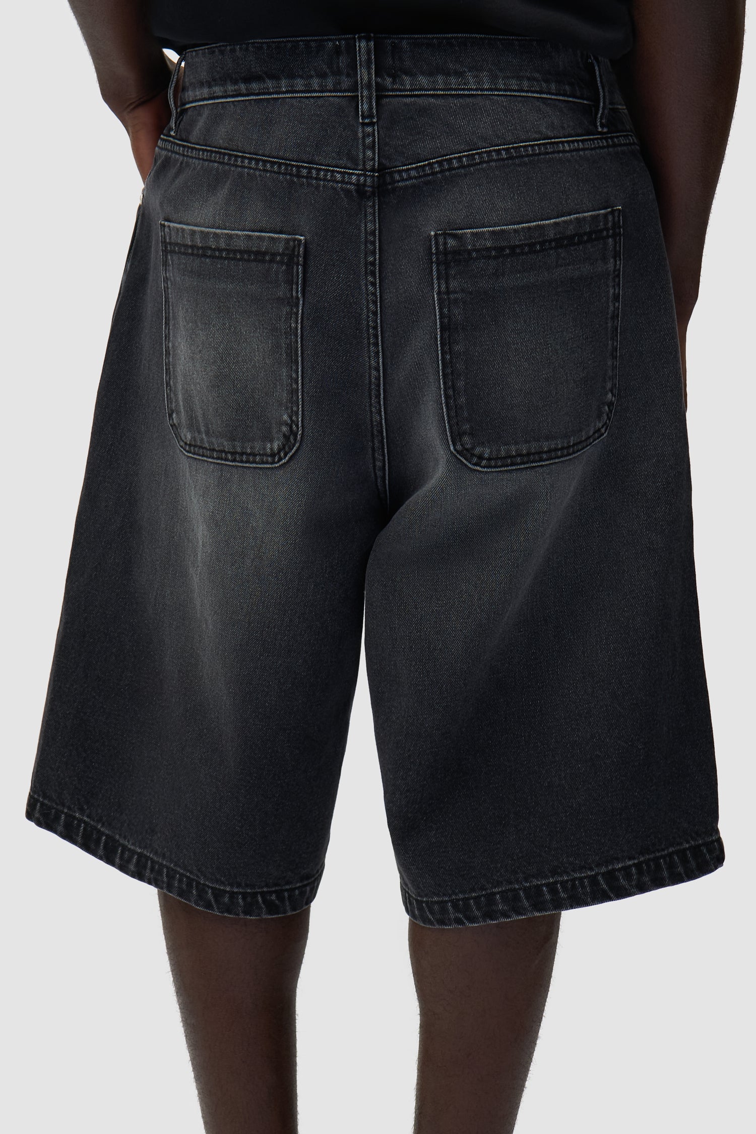 Short en denim à poches rondes, couleur noir délavé, porté par un mannequin, vue de dos à mi-corps