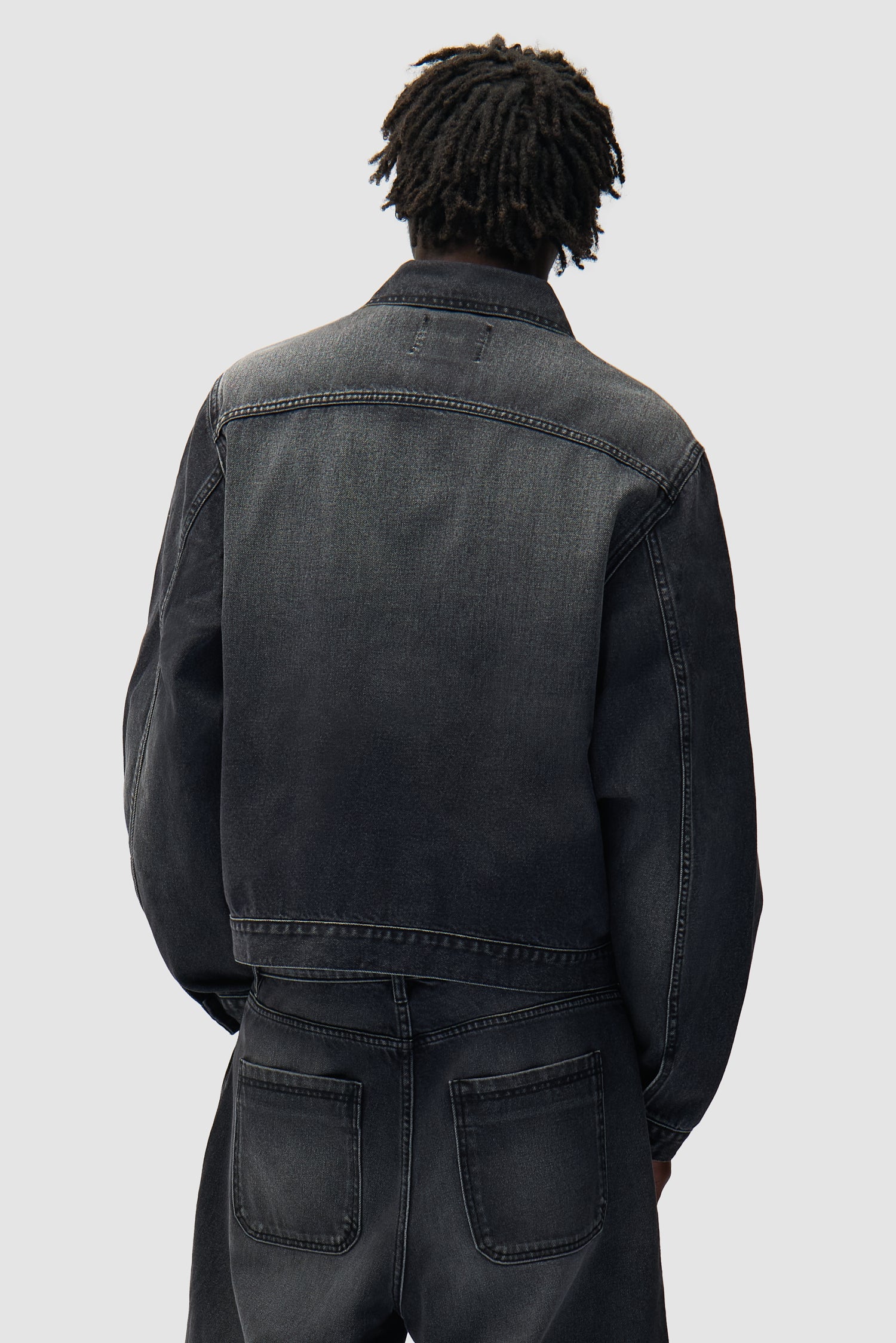 Veste en denim à poches plissées, couleur noir délavé, portée par un mannequin, vue de dos à mi-corps